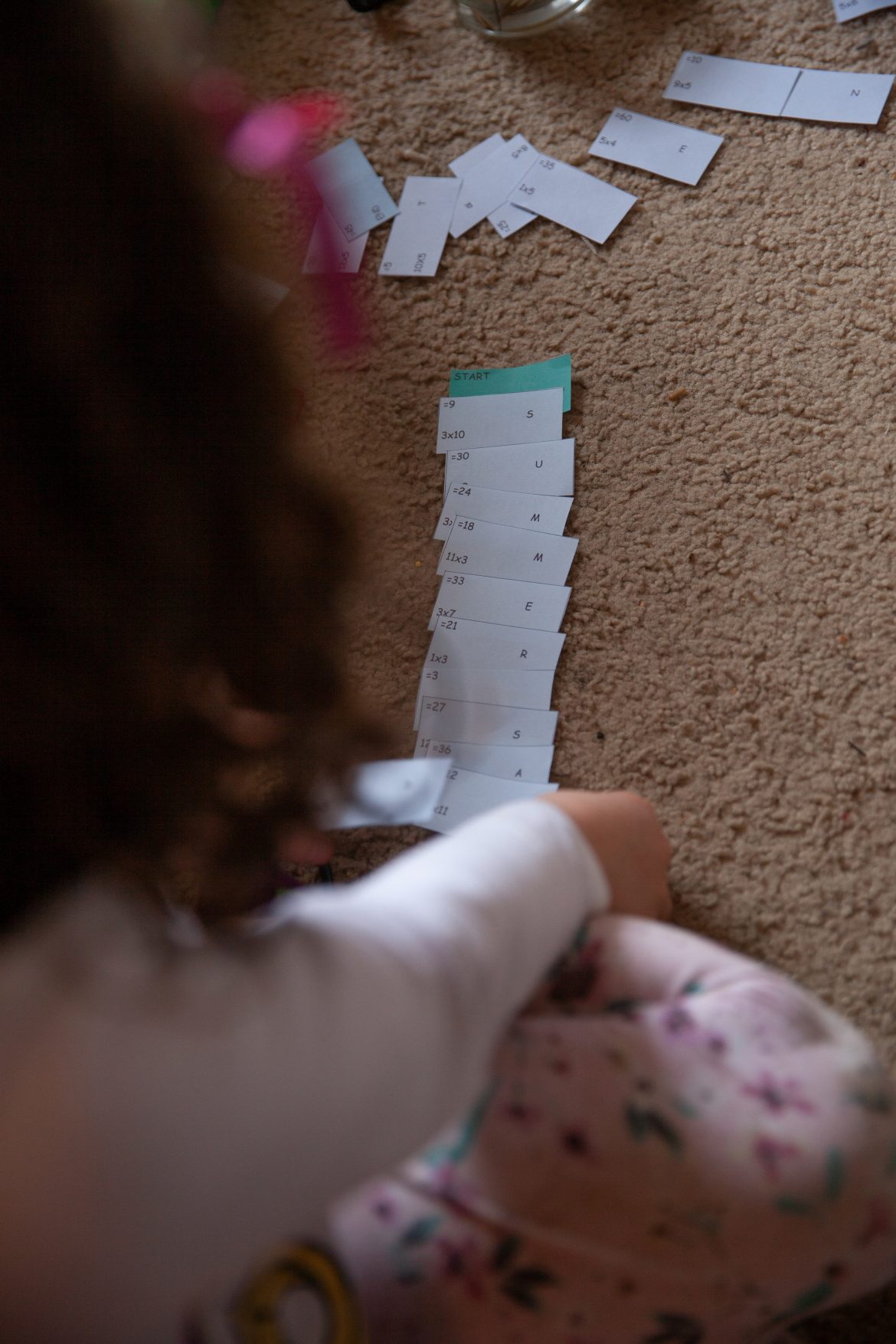 Young girl organising slips of paper with math sums, answers and a letter on them to form a word