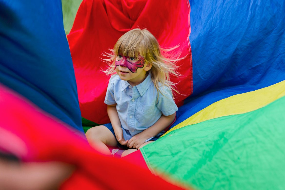Little Child Sitting on a Colorful Parachute