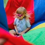 Little Child Sitting on a Colorful Parachute