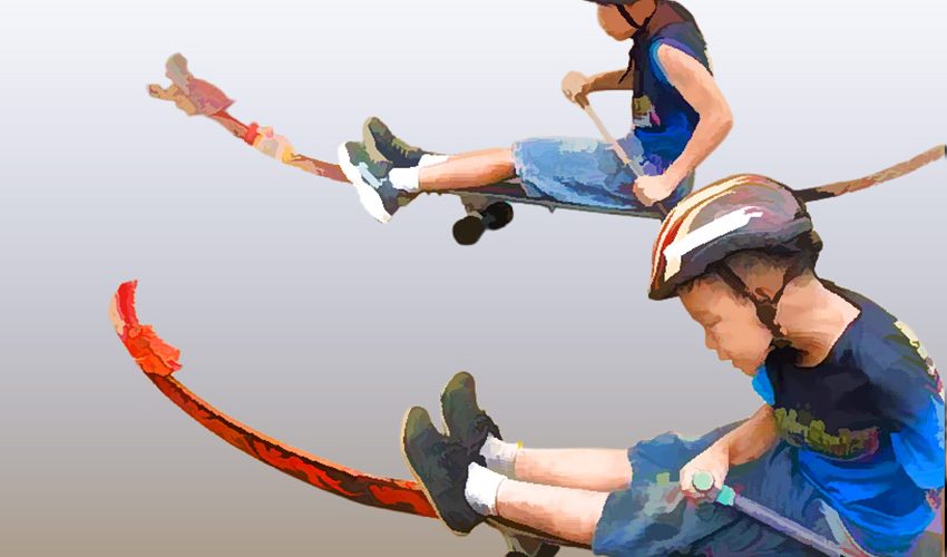Two children each sitting on a skateboard with decorative extensions to look like dragon boats, propelling themselves using sticks.